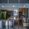 Denham Outdoor Swan Neck Wall Light mounted above a restaurant entrance with warm brass finish and glass shade illuminating exterior seating area.