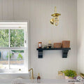 Denham Outdoor Swan Neck Wall Light in polished brass mounted on white paneled wall above black shelf in bright kitchen setting