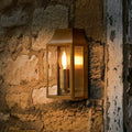 Pooky Crail Wall Light solid brass outdoor lantern mounted on textured stone wall glowing warmly at night