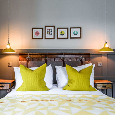 Vienna Pendant Light with industrial design hanging over a bed with yellow pillows and wooden headboard in a modern bedroom