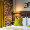 Vienna Pendant Light hanging over bedside table in cozy rustic bedroom with stone wall and green accents