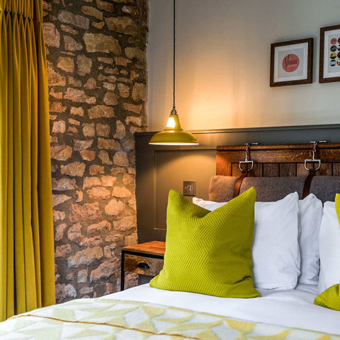 Vienna Pendant Light hanging over bedside table in cozy rustic bedroom with stone wall and green accents