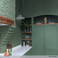 Mono prismatic pendant light with vintage prismatic glass shade hanging in green kitchen interior above white countertop.