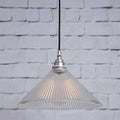 Rebell Prismatic Glass Pendant Light with a conical prismatic glass shade hanging against a white brick wall background