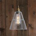 Kairi Glass Pendant light with clear cone-shaped glass shade and exposed filament bulb against wooden background