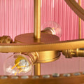 Close-up of the brass frame and light bulbs in the Pooky Athena Chandelier pendant light with a pink background
