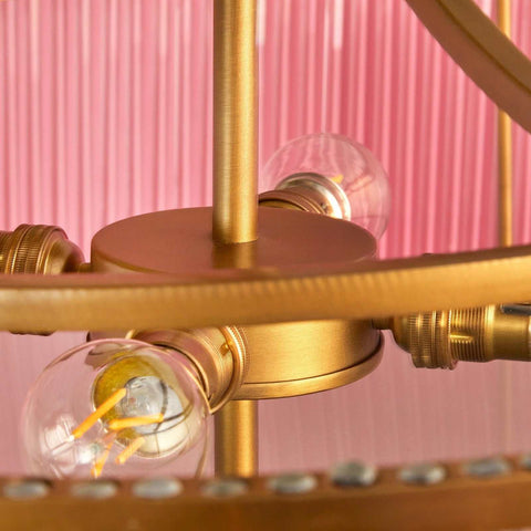 Close-up of the brass frame and light bulbs in the Pooky Athena Chandelier pendant light with a pink background