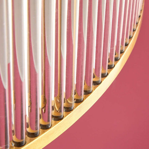 Close-up view of Pooky Athena Chandelier brass frame with delicate glass rods against a pink background