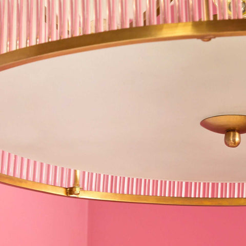 Close-up of Pooky Athena Chandelier pendant light with brass frame and glass rods against a pink background