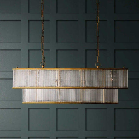 Odin Chandelier pendant light with double-tiered brass frame and handcrafted glass rods hanging against dark paneled wall