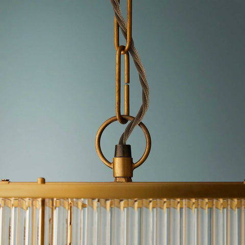 Close-up of golden brass frame and hanging chain of the Odin Chandelier pendant light with handcrafted glass rods