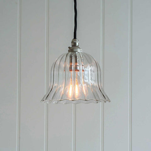 Small Bodium Pendant Light with clear ribbed glass shade and flexible black cord hanging against white paneled wall
