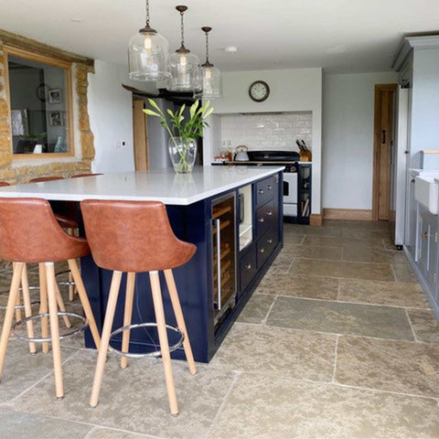 Hythe Large Clear Glass Shade pendant lights hanging over a modern kitchen island with brown leather bar stools and stone tile flooring
