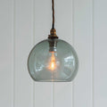 Soho Medium Smoked Glass Shade pendant light with a warm glowing bulb and twisted cord hanging against a white paneled wall