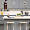 Contemporary large clear glass knot pendant lights hanging above a modern kitchen island with grey cabinetry and wooden stools