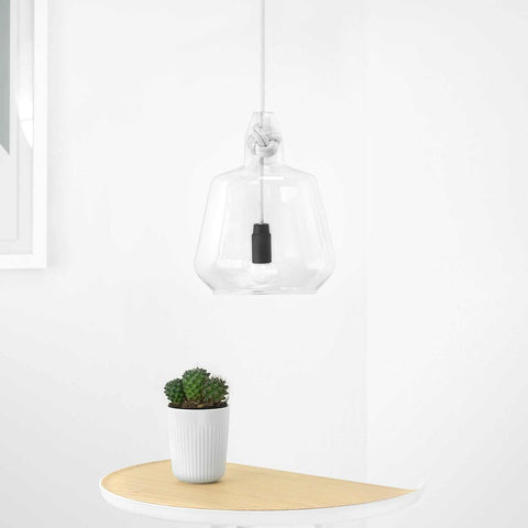 Contemporary large clear glass pendant light with hand-blown shade and knot detail hanging above wooden table with small plant.