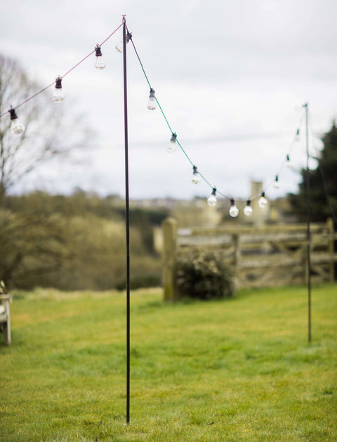 Steel festoon poles for outdoor lighting with bull horn design and pointed base in garden setting