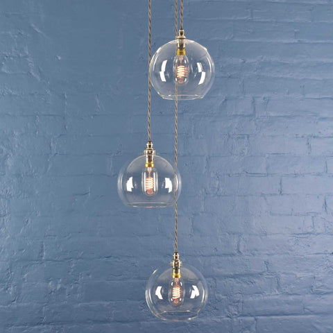 Soho medium clear glass three globe cluster pendant light with brass fittings against blue brick wall