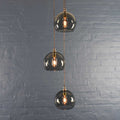 Soho Medium Smoked Glass 3 cluster pendant light with hand-blown smoked glass globes and twisted cords against a gray brick wall background