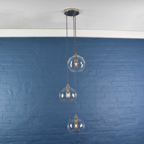Soho Medium Clear Glass 3 cluster pendant light with hand-blown glass globes and adjustable drop length, hanging against blue wall