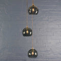 Soho small smoked glass shade cluster pendant light with three hand-blown globes and adjustable cords against a gray brick wall background