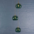 Soho small teal glass shade cluster pendant light with three hand-blown globes hanging against a blue brick wall