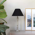 Antique grey Whitwell Wooden Table Lamp with handcrafted base and black fabric shade on wooden table near plant and framed landscape photos