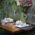 Zafferano Poldina Micro rechargeable black table lamp on wooden dining table with plates, cutlery, glasses, and floral centerpiece outdoors