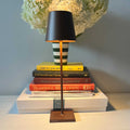 Zafferano Poldina Pro rechargeable rust-colored table lamp with sleek design on stacked books and a green-striped vase with white flowers in the background