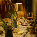 Zafferano Poldina Pro rechargeable gold table lamp on a dining table with flowers and wine glass, providing warm ambient lighting