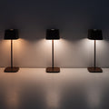 Three Zafferano Ofelia Pro rechargeable table lamps with black shades showing different warm to cool lighting settings against a plain wall
