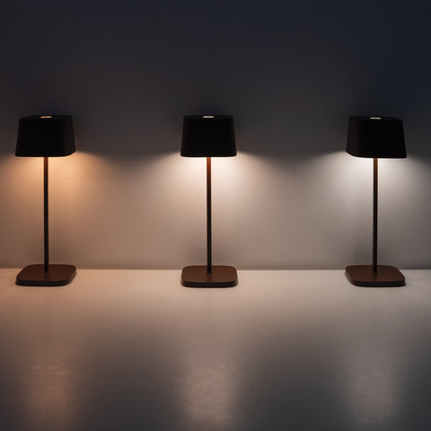 Three Zafferano Ofelia Pro rechargeable table lamps with black shades showing different warm to cool lighting settings against a plain wall
