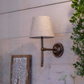 Finberry fabric shade Lupin wall light with beige fabric shade and antique brass fitting mounted on light gray wooden wall.