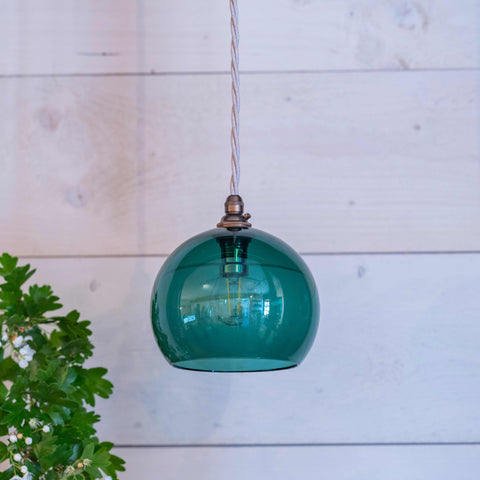 Soho small teal hand-blown glass globe pendant light hanging against a white wooden wall