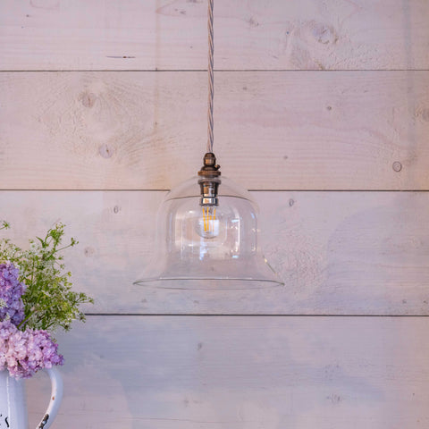 Bodium Medium Clear glass bell-shaped pendant light hanging in front of wooden wall with floral arrangement nearby