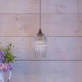Camber Small Ribbed Glass Shade pendant light with fluted clear glass and vintage-style bulb hanging against rustic wooden wall