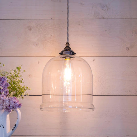 Hythe Medium Clear Glass pendant light with exposed bulb and vintage-style twisted cord hanging against wooden wall