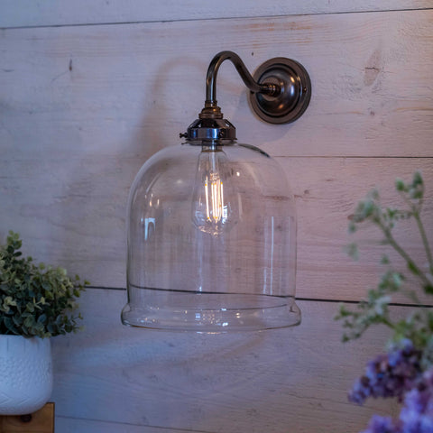 Hythe Medium Clear Glass shade wall light with antique brass finish mounted on wooden wall