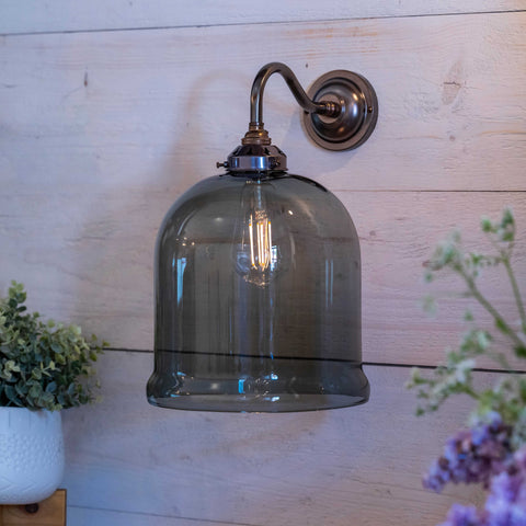 Hythe Medium Smoked Glass bell-shaped wall light with antique brass finish mounted on wooden wall