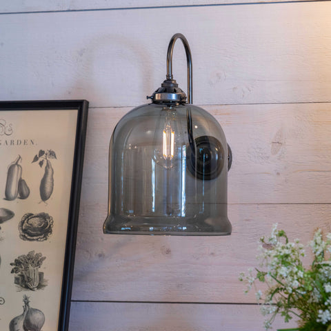 Hythe Medium Smoked Glass shade wall light with bell-shaped smoked glass and antique brass finish mounted on wooden wall