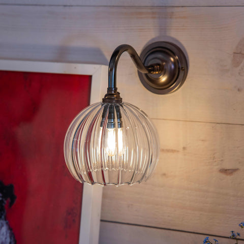 Soho Small Ribbed Glass shade wall light with antique brass finish and soft glowing bulb mounted on wooden wall