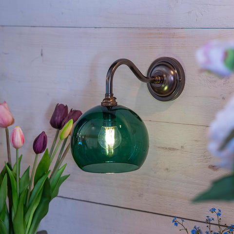 Soho small teal glass shade wall light with bronze finish mounted on wooden wall near flowers