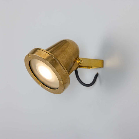 Thames Outdoor Spot Light in raw brass finish mounted on wall with adjustable swivel for outdoor use.