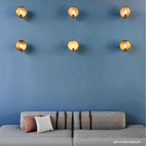 Chulainn Dish Wall Light vintage brass dish wall lamps with walnut arms mounted on blue wall above gray sofa with cushions