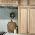 Chulainn Dish Wall Light with antique brass finish mounted on marble kitchen backsplash next to wooden cabinetry