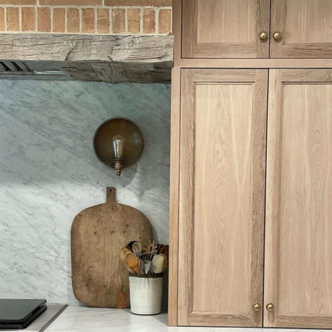 Chulainn Dish Wall Light with antique brass finish mounted on marble kitchen backsplash next to wooden cabinetry
