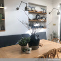 Dale Adjustable Wall Light illuminating a modern dining area with wooden table, decorative plants, and wall shelves with plates.