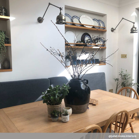 Dale Adjustable Wall Light illuminating a modern dining area with wooden table, decorative plants, and wall shelves with plates.