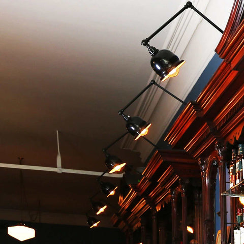 Dale Adjustable Wall Light in black with pivoting heads illuminating a wooden shelving unit