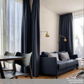 Dale Adjustable Wall Light in brass finish mounted above a navy blue sofa in a modern living room with dark curtains and wooden flooring.